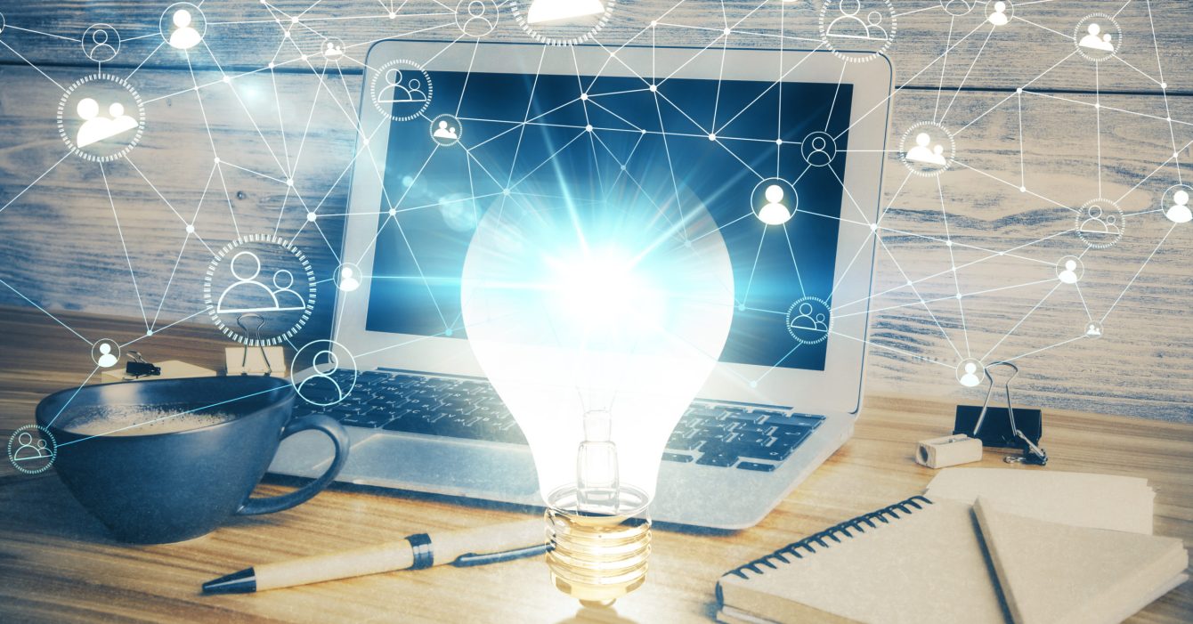 Computer on desktop in office with bulb icon hologram. Double exposure. Concept of idea.
